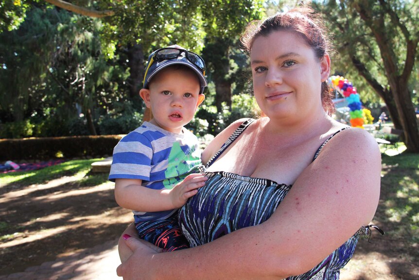 A woman holds a toddler in a park.