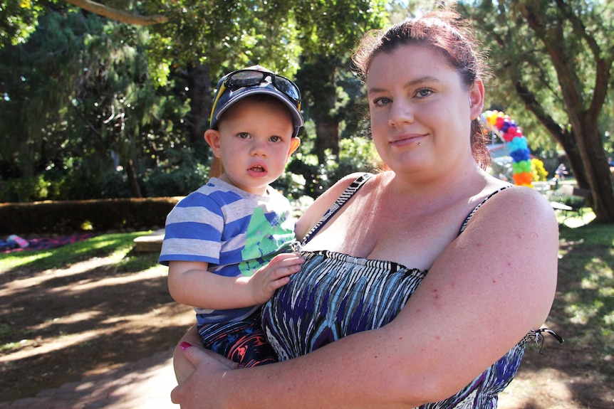 A woman holds a toddler in a park.