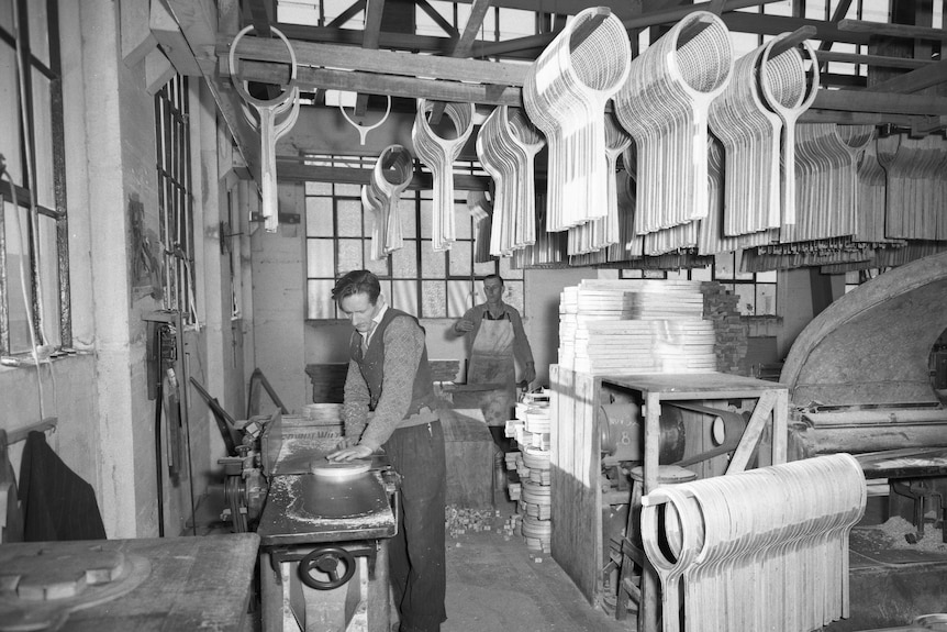 A black and white photo of a man standing in a tennis racquet factory
