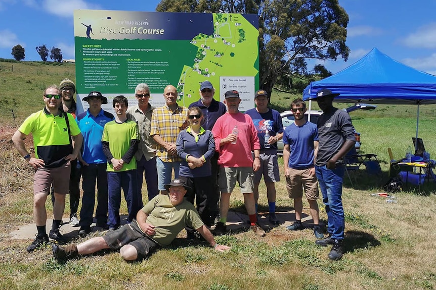 A group of disc golf players pose for a group shot in front of the course info board.