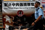 A policeman walks past a protest banner that says "stop forced organ harvesting in China".