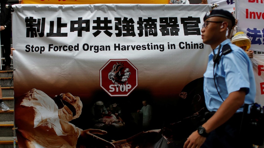 A policeman walks past a protest banner that says "stop forced organ harvesting in China".