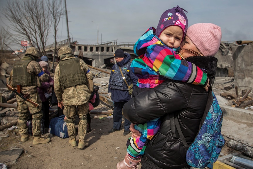 A woman holds a child next to a destroyed bridge