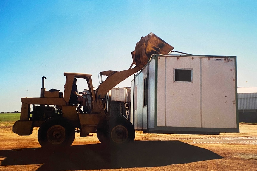 A tractor carrying an old donga on a farm.