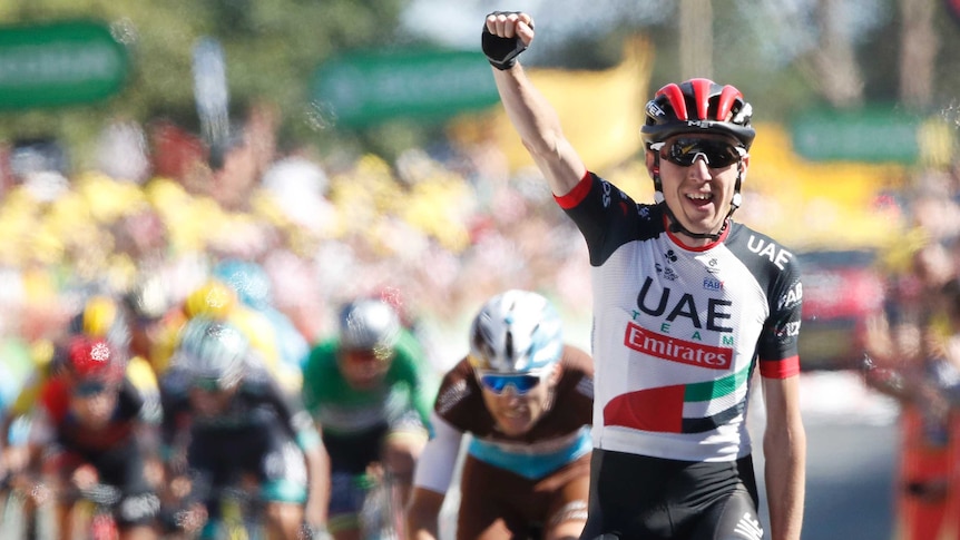 Dan Martin rides up a hill with his hand in the air, other cyclists are seen in the background