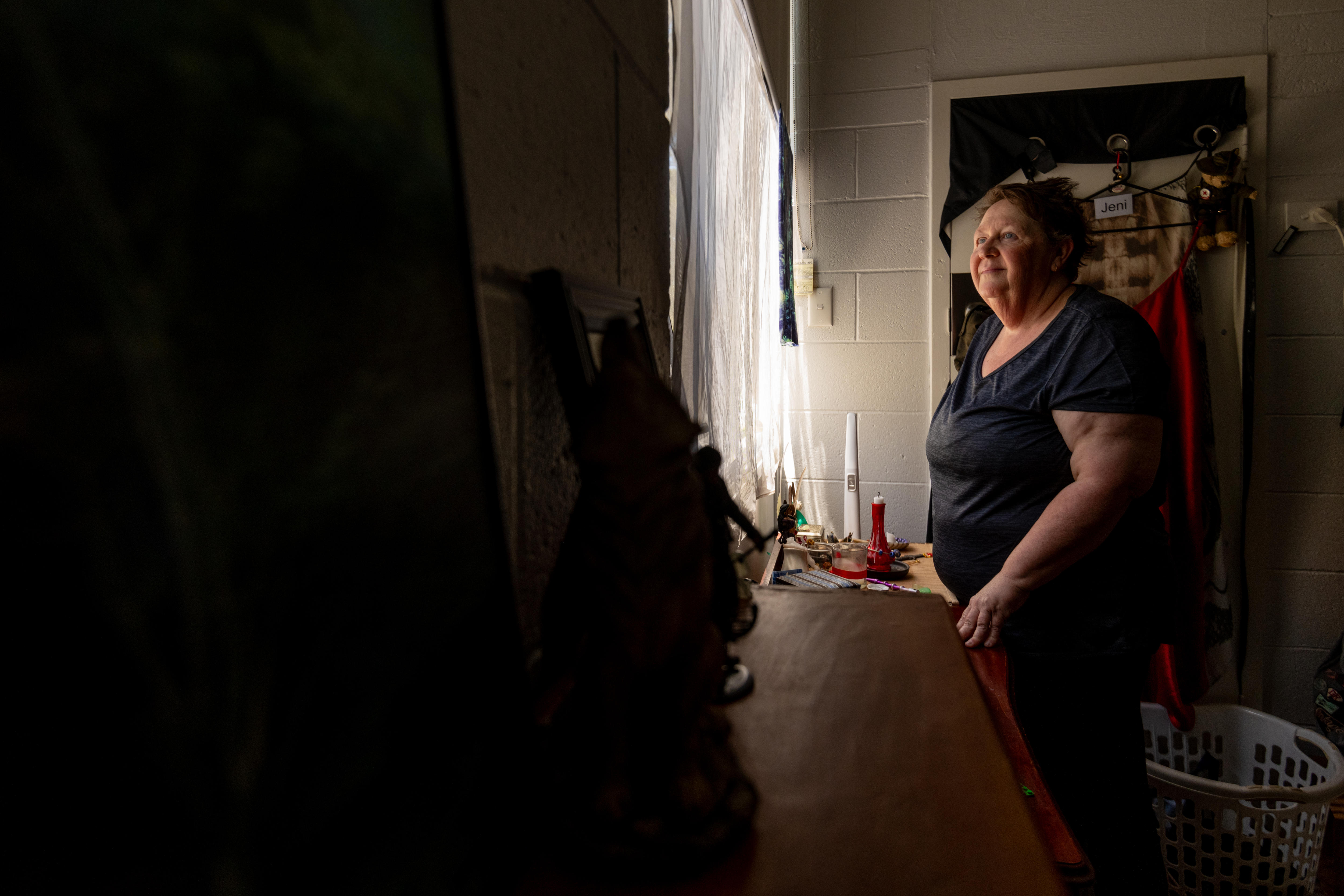 A woman in a dark room looks out a window