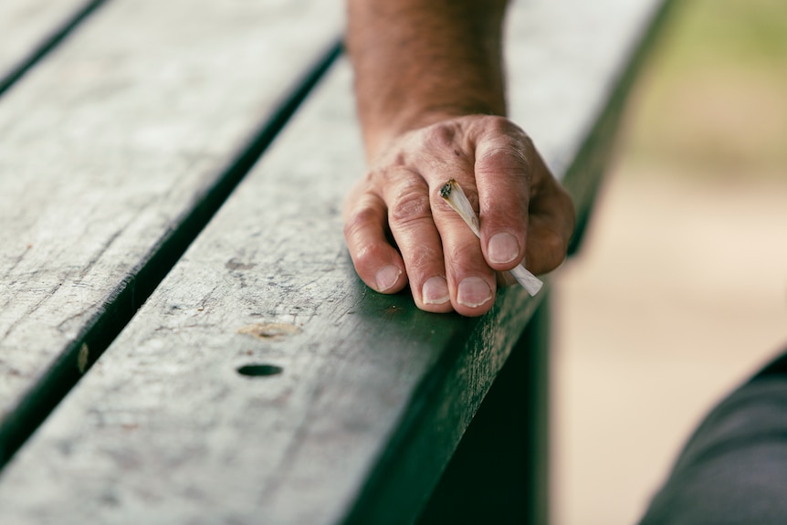 A close-up photograph of a hand holding a rolled cigarette.