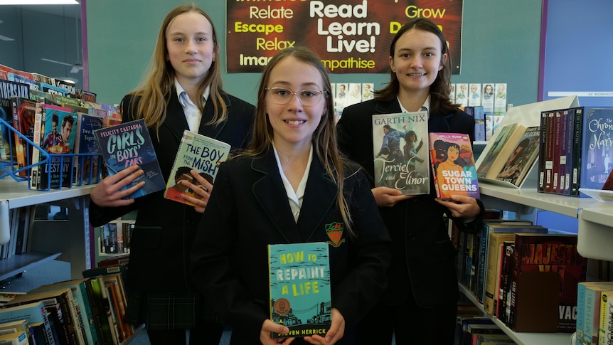 Three girls holding shortlisted books in the school library