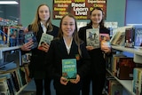 Three girls holding shortlisted books in the school library