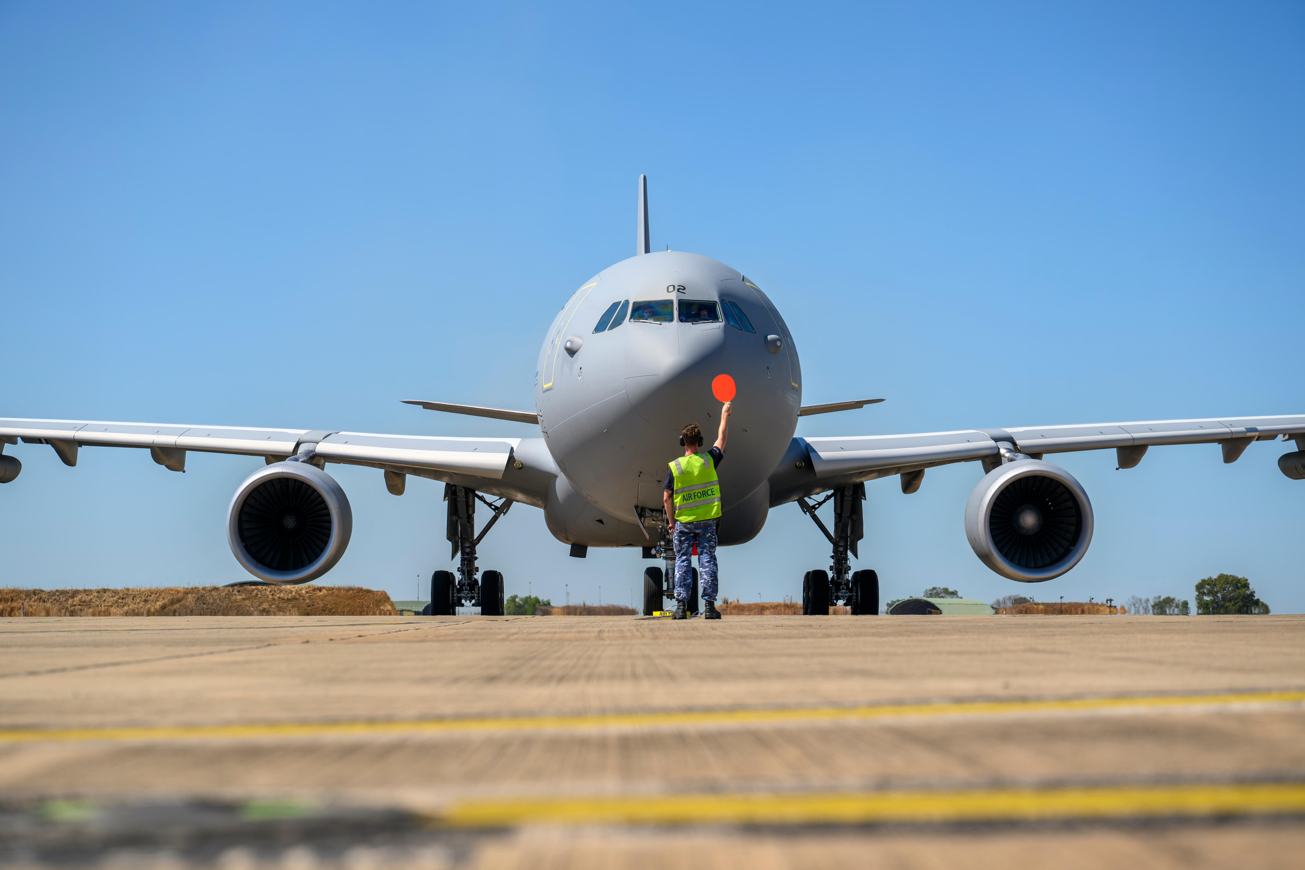A man holds a round red sign in front of a transport plane.