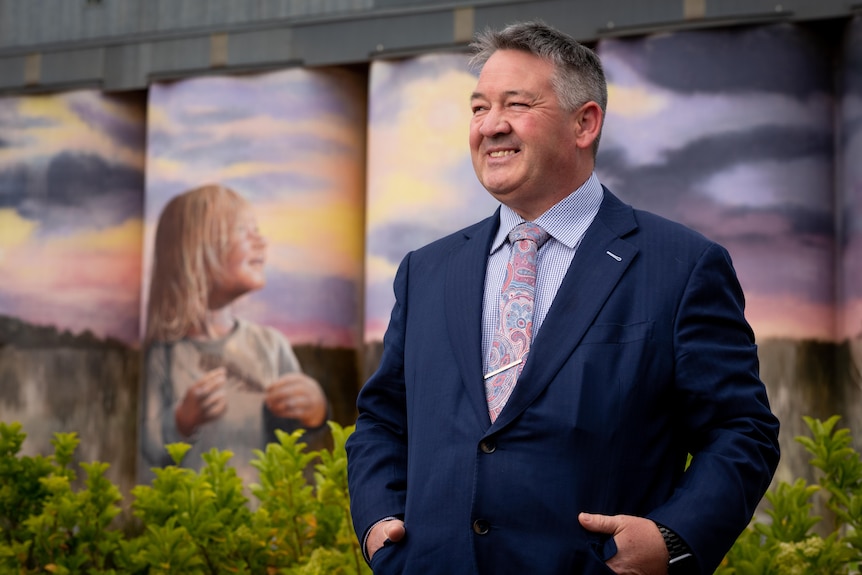 Man in suit stands in front of silo art.