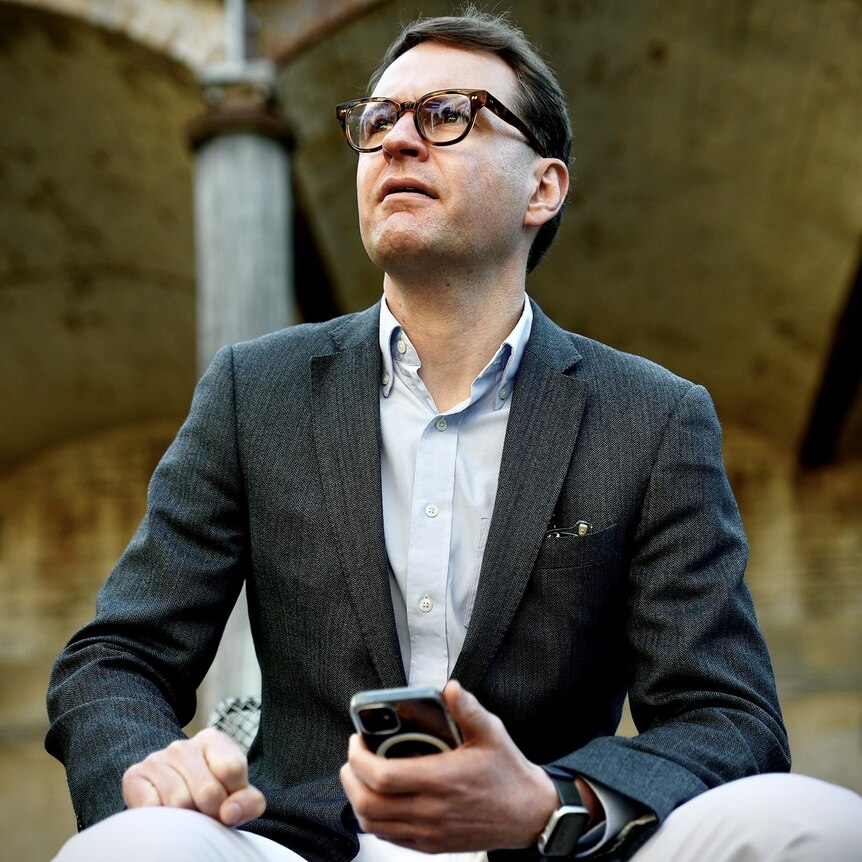 A Caucasian man wearing glasses, holding a mobile phone.