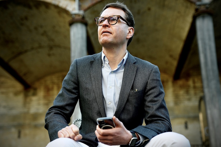 A Caucasian man wearing glasses, holding a mobile phone.