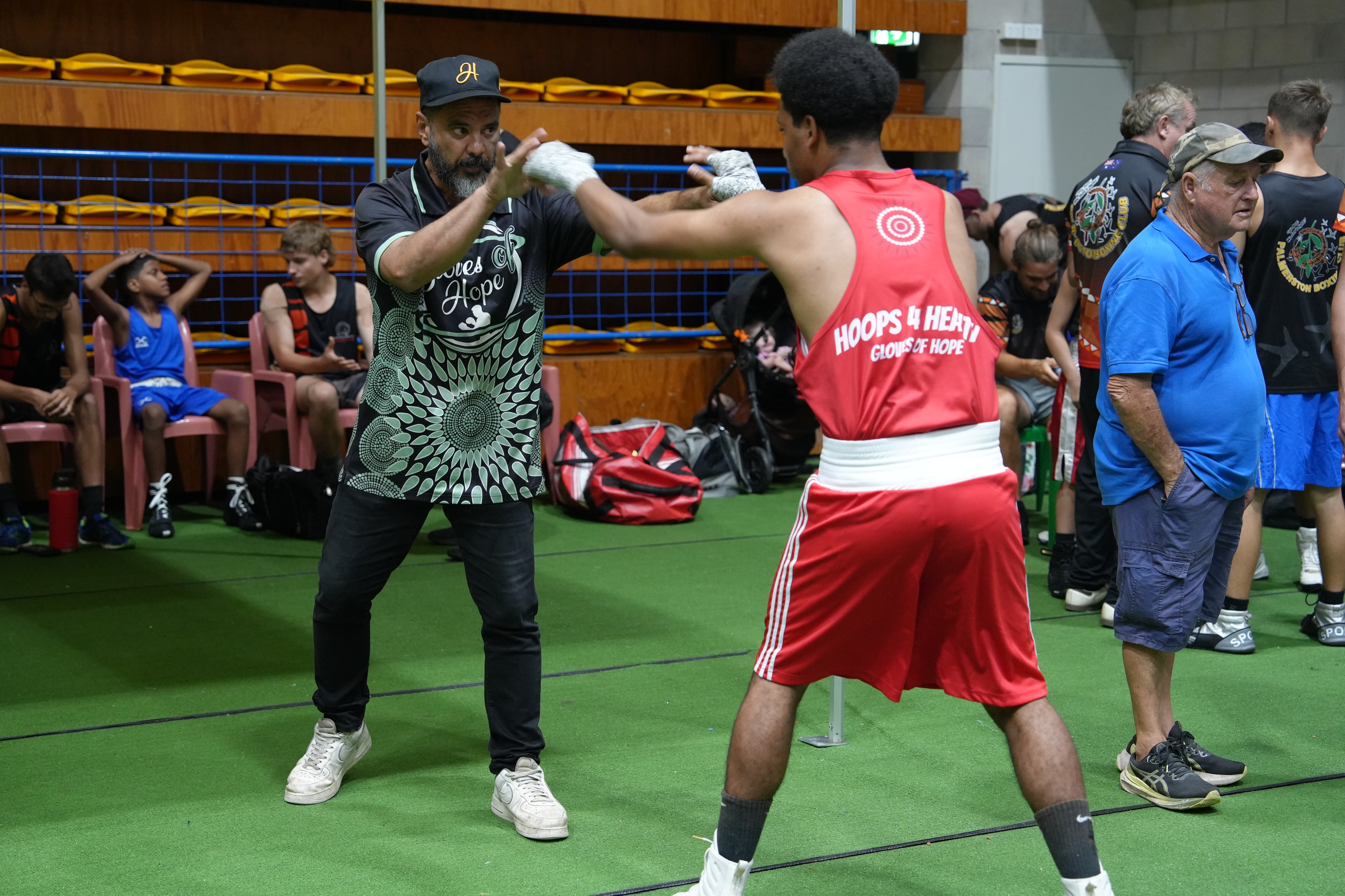 Matthew Bonson has brown skin and a beard, his hands are up in front as he blocks a young boxer's punches during warm-up.