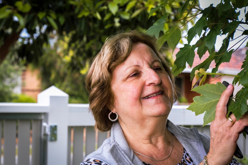 A woman smiles as she inspects a leaf on a tree