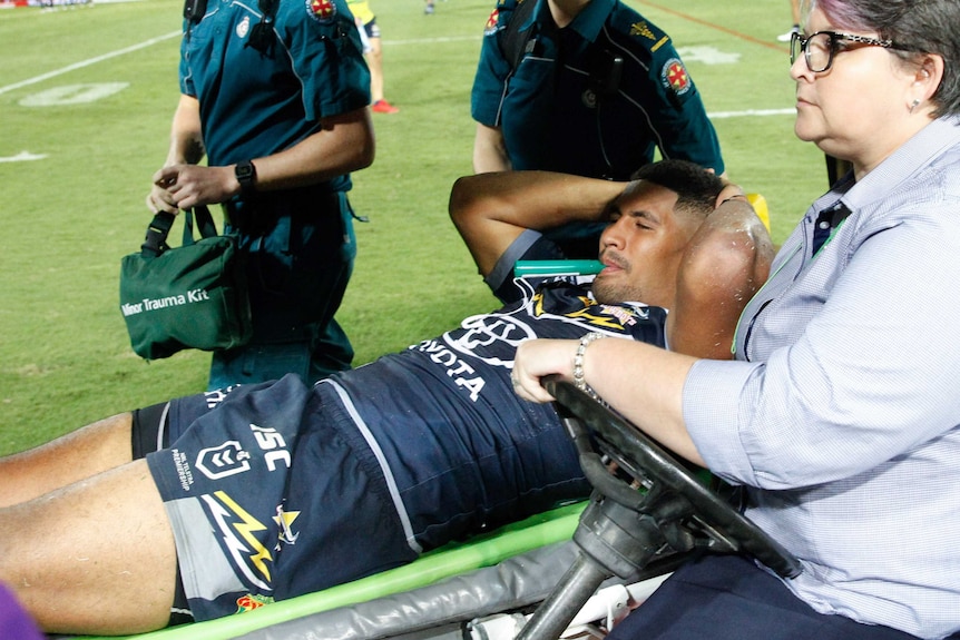 Nene Macdonald holds his head as he is carried off the field on a stretcher with paramedics walking alongside