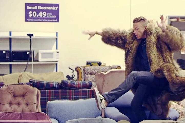 A man in a fur coat jumps across second hand furniture