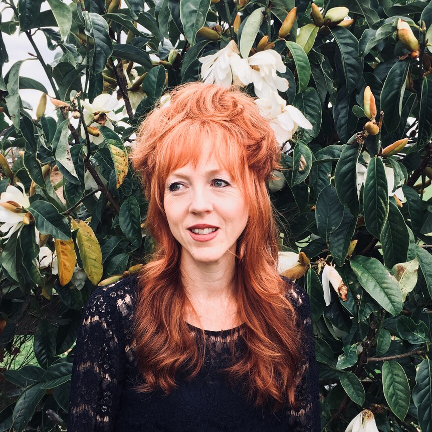 Red-haired lady standing in front of greenery.