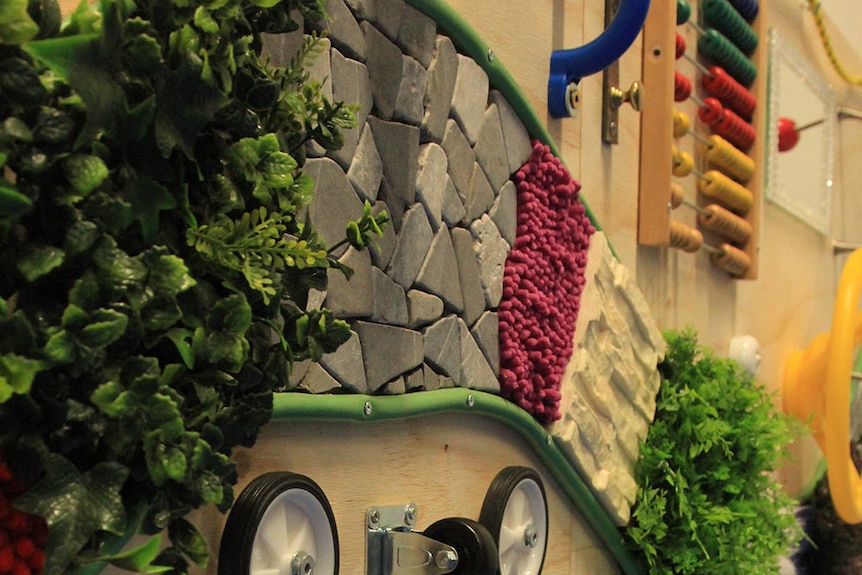 Various materials on a wall including coloured beads, wheels, stones and plastic leaves.