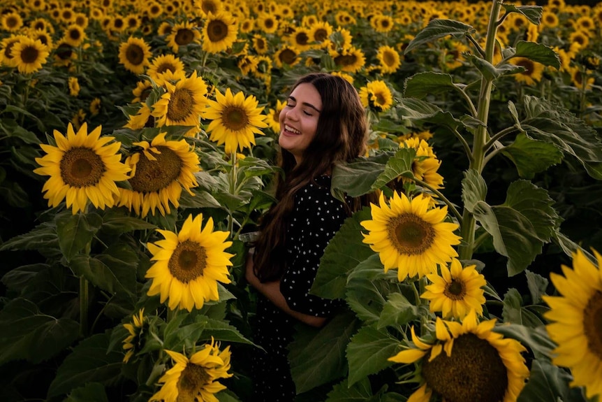 A woman in a field full of big flowers with her eyes closed and smiling. 