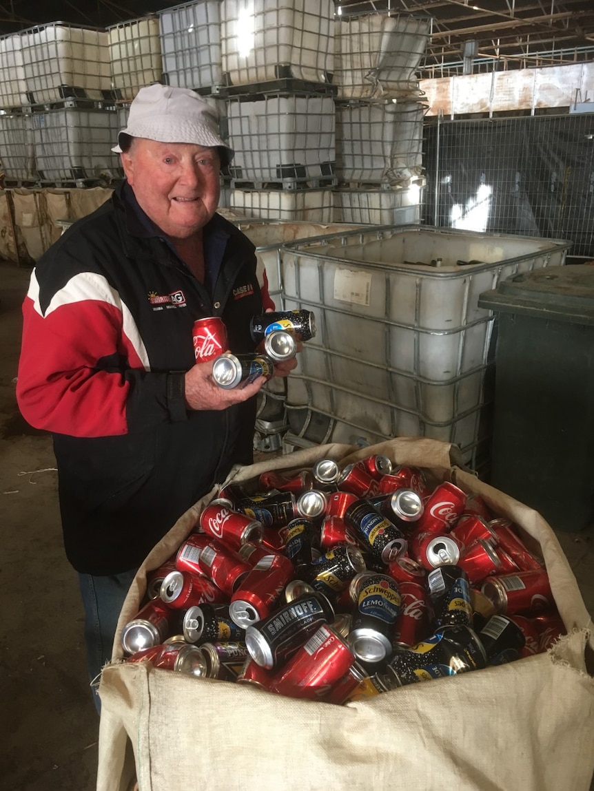 81-year-old Robert Jolley holds four soft drink cans in his hands while standing in a recycling facility.