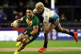Australia's Valentine Holmes holds a football and runs as a Fijian player leans to tackle him from behind. 