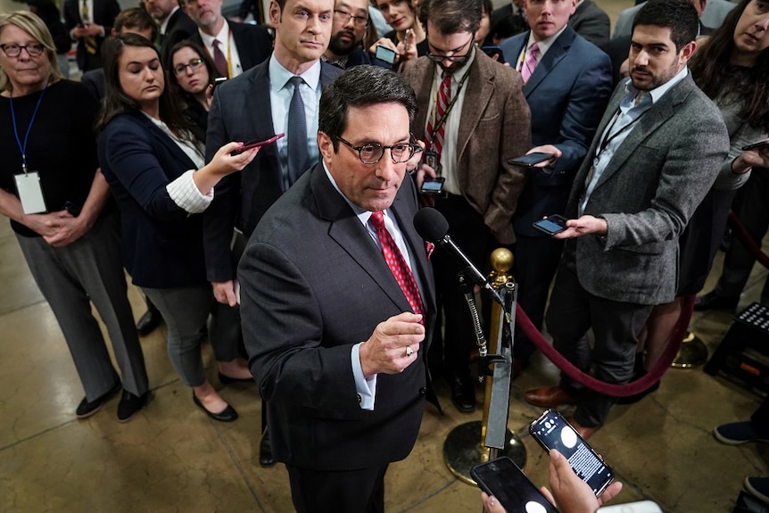 A man standing in the middle of reporters and speaking