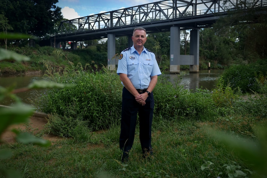 A man in a blue uniform standing on grass with a bridge and river behind him
