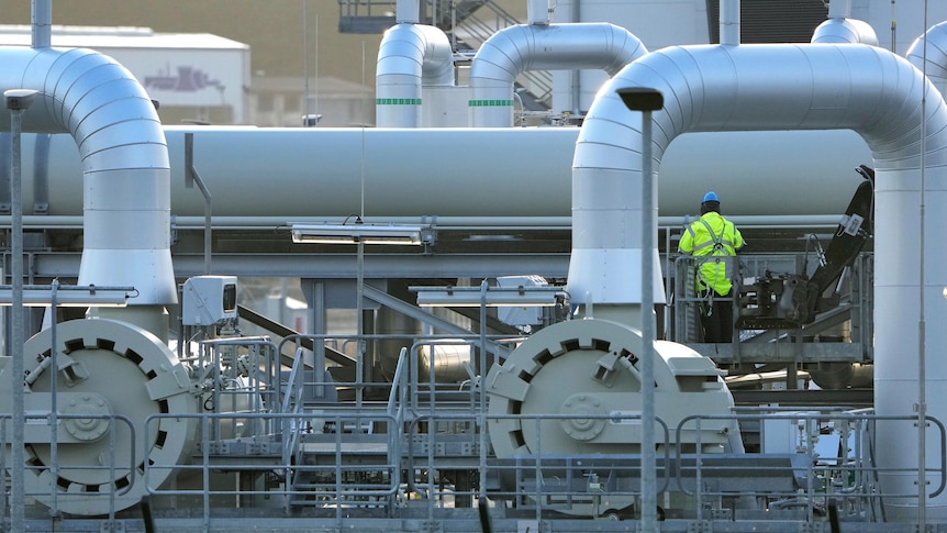 A man in high vis stands on a network of large steel pipes.