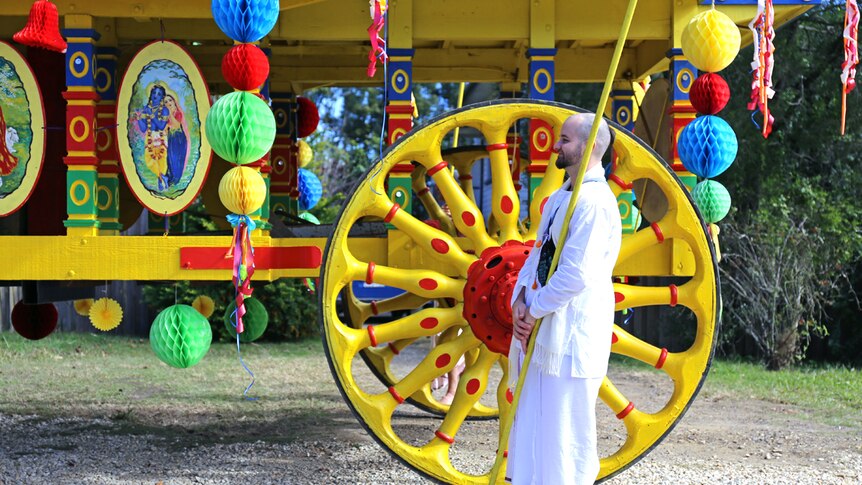 Hare Krishna devotee stands next to chariot wheel