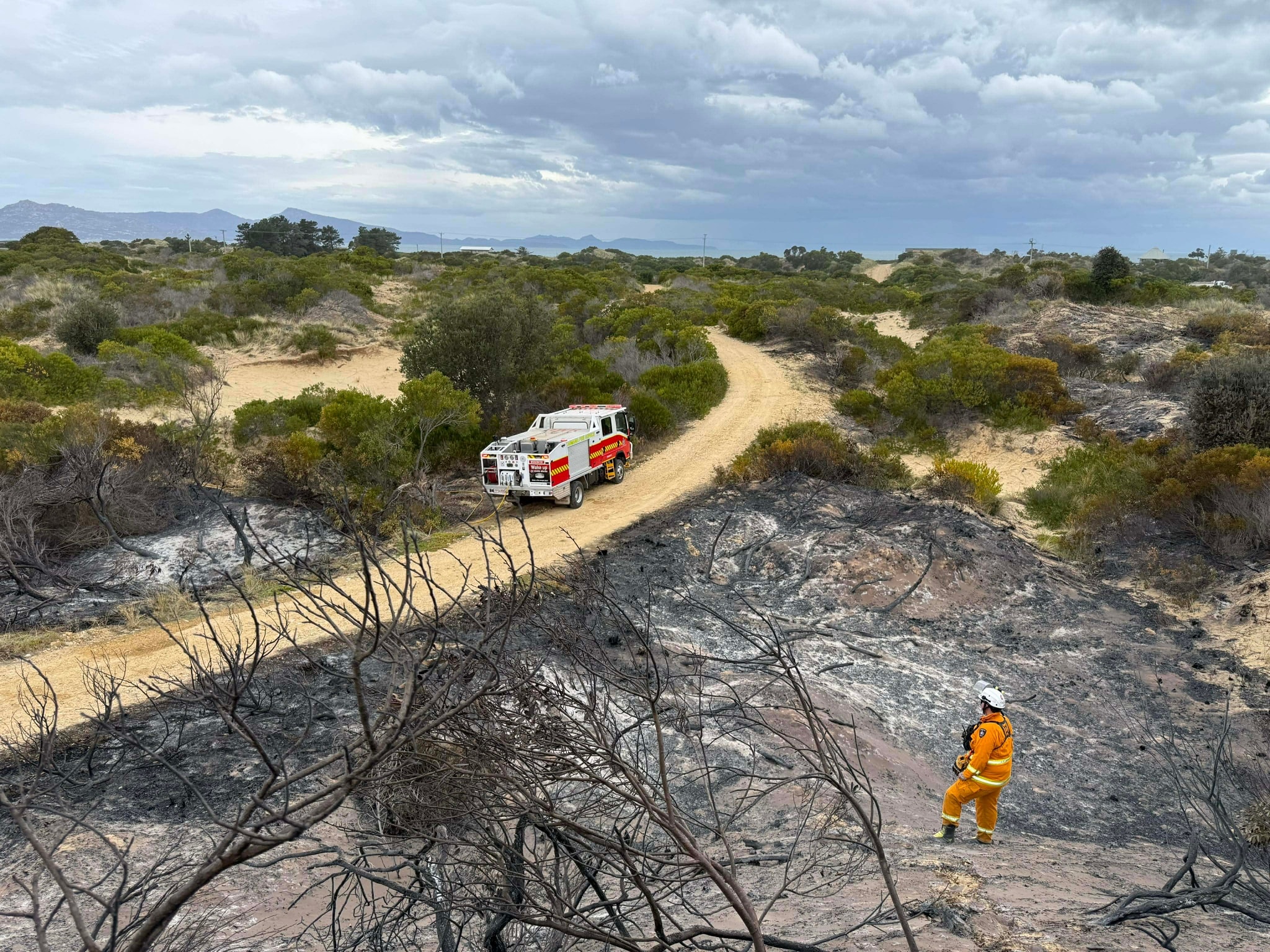 Vista de ángulo alto de bombero y camión en un paisaje rural quemado.