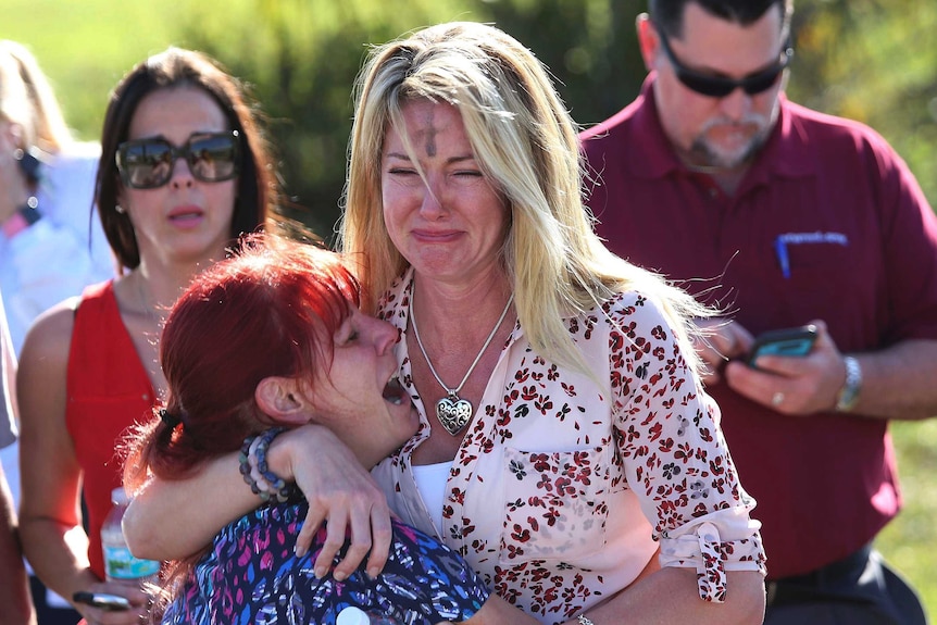 Two women, one with an Ash Wednesday cross on her forehead, cry at the Florida school where 17 people were shot dead.