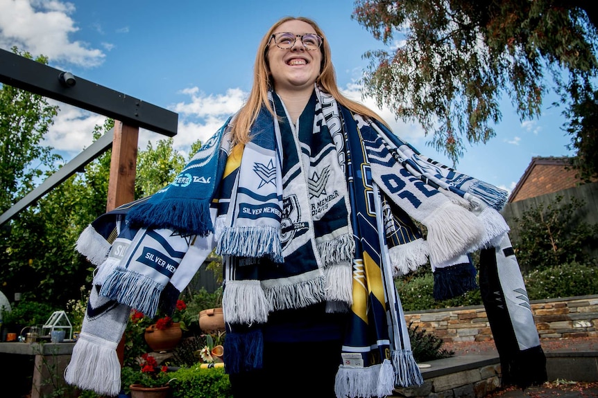 A young woman stands with several Melbourne Victory scarves around her neck.