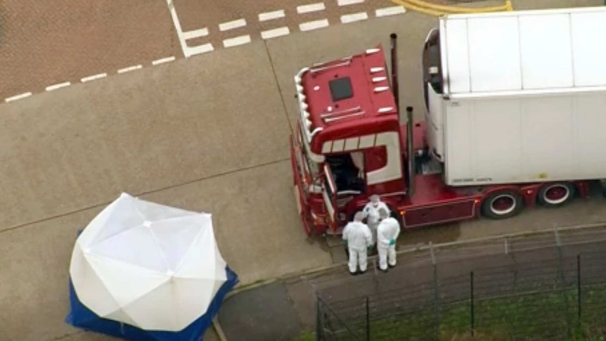 Forensic workers are seen from above standing next to a red truck with a white body. A tent has been erected to the left.