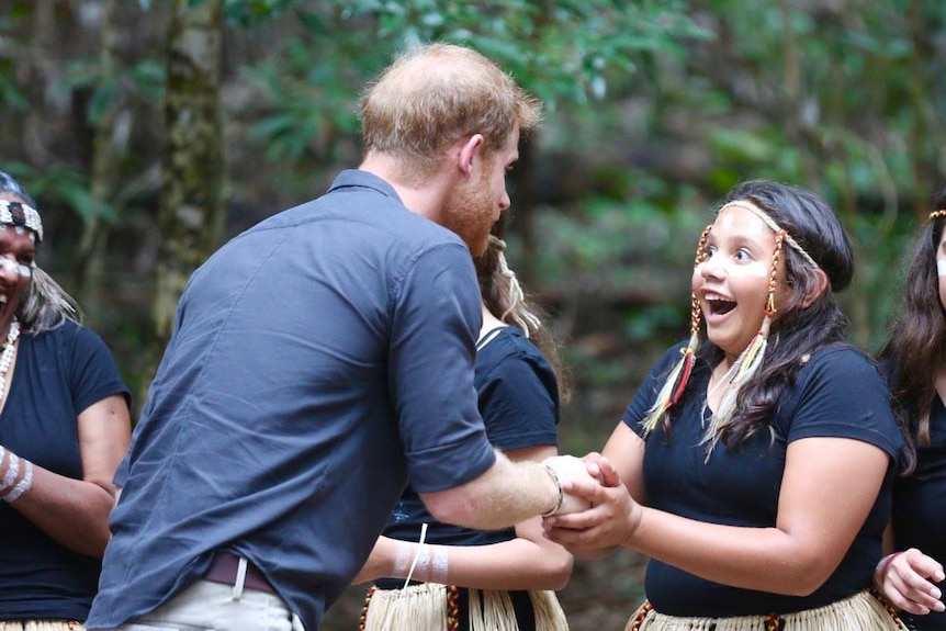 A young girl with a big smile on her face shaking hands with Prince Harry