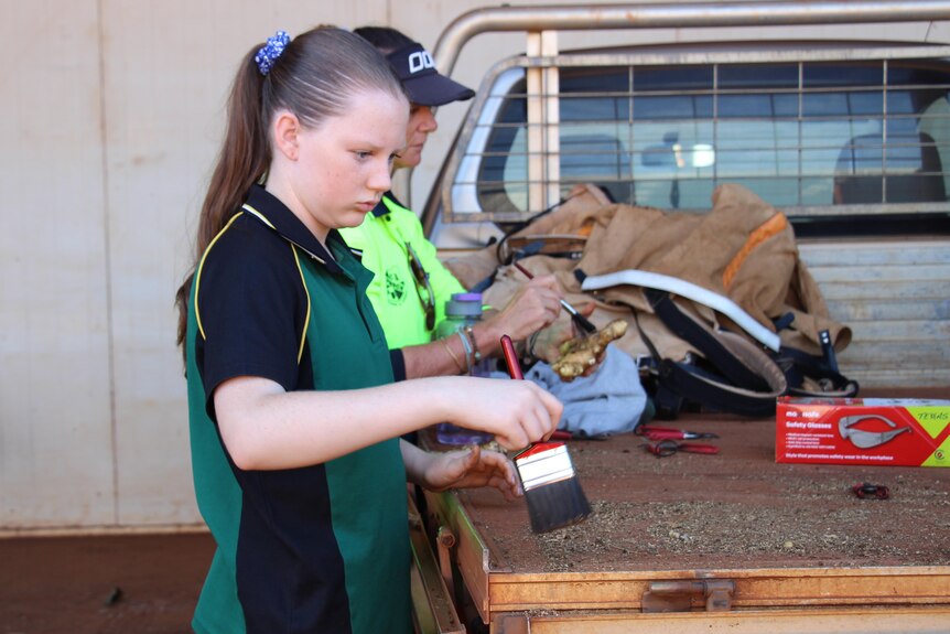 A young girl in a school uniform holding a brush against a ute tray