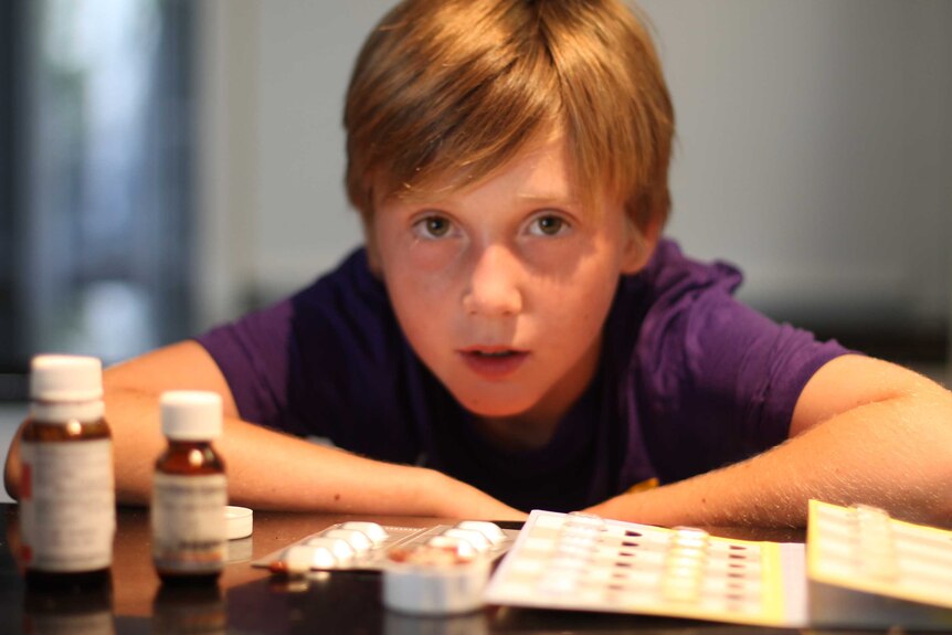 Kai Barton crouching down behind some of the medications he takes