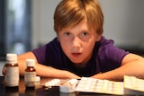 Kai Barton crouching down behind some of the medications he takes