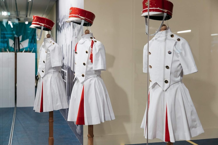 White and red costumes for Cherbourg marching girls hand on stands in a display.
