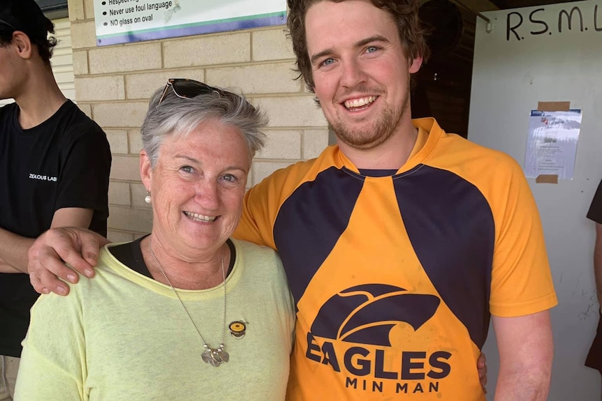 Young man in gold and brown football guernsey, arm around smiling mum.