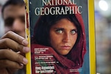 The owner of a book shop shows a copy of a magazine with the photograph of Afghan refugee woman Sharbat Gulla.