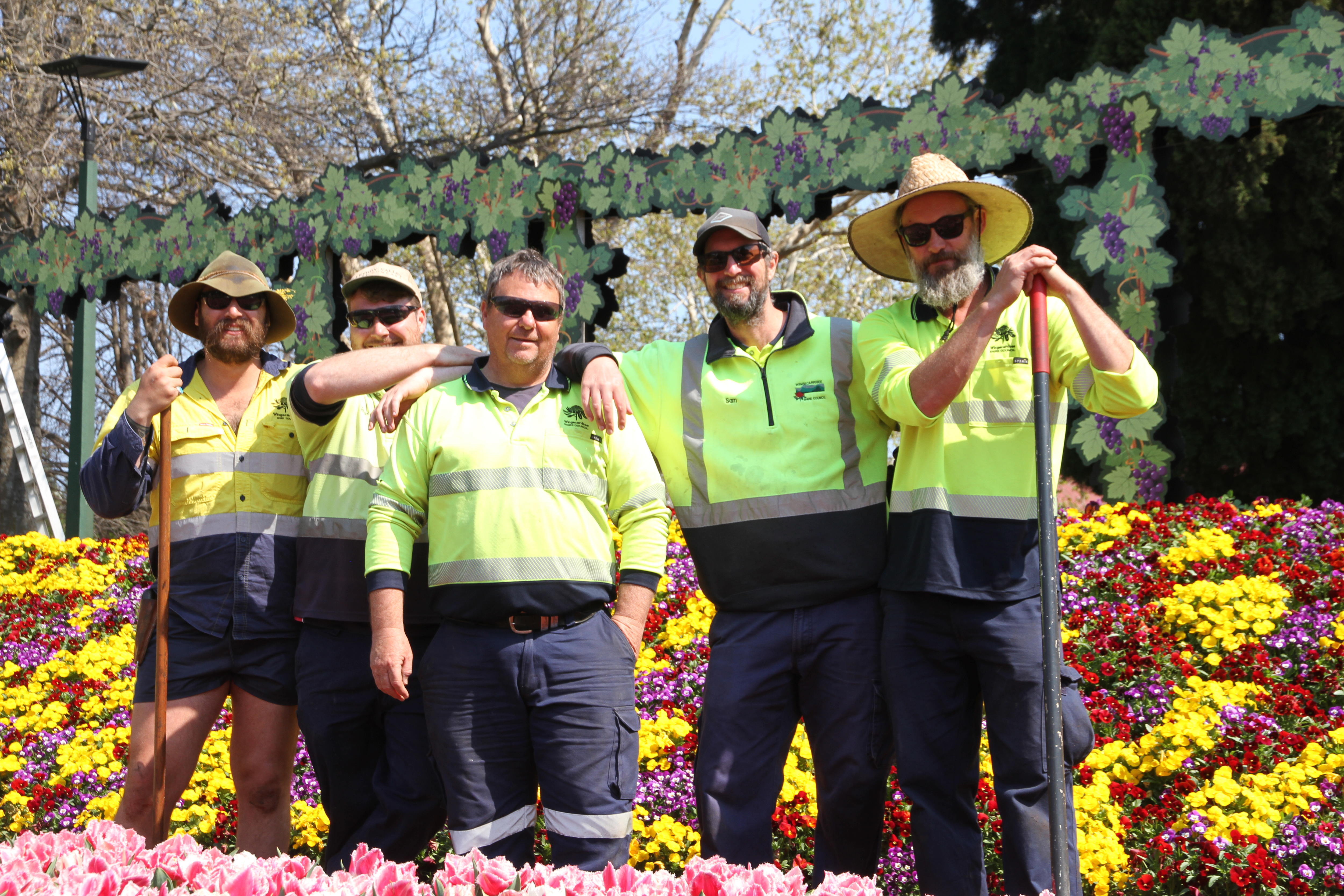 A group of men stand with tools in a flower garden