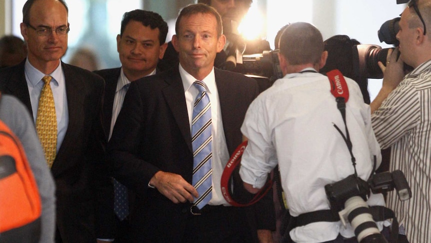 Tony Abbott strides down a busy corridor, surrounded by photographers