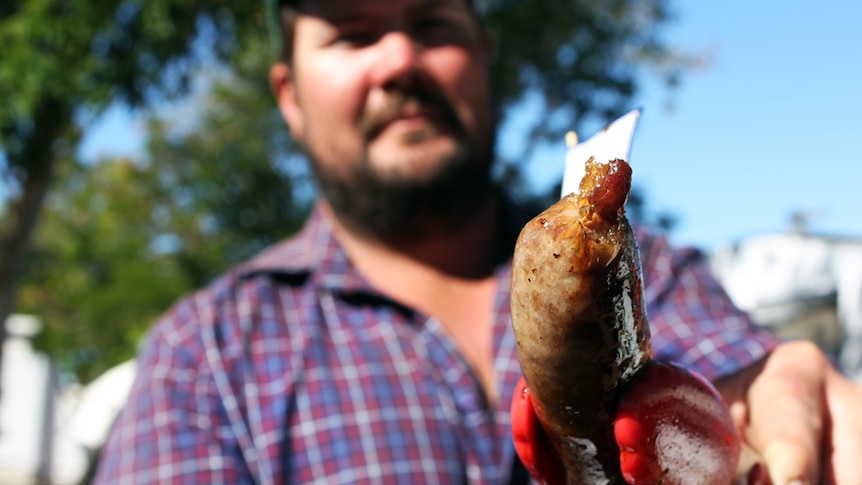 Brad Haydon holds one of his sausages at Cloncurry sausage sizzle-off