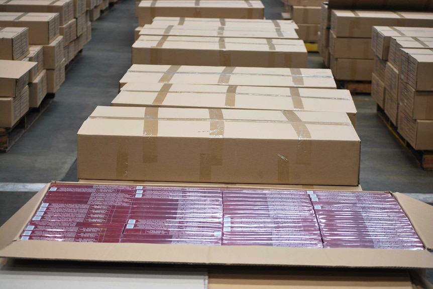 Long cardboard boxes lie stacked on the ground with one opened showing smaller red cartons of cigarettes.