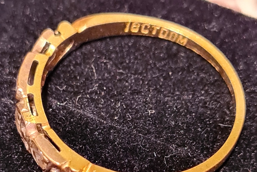 A gold ring with five diamonds inscribed with the stamps 18ct sits on a black cloth