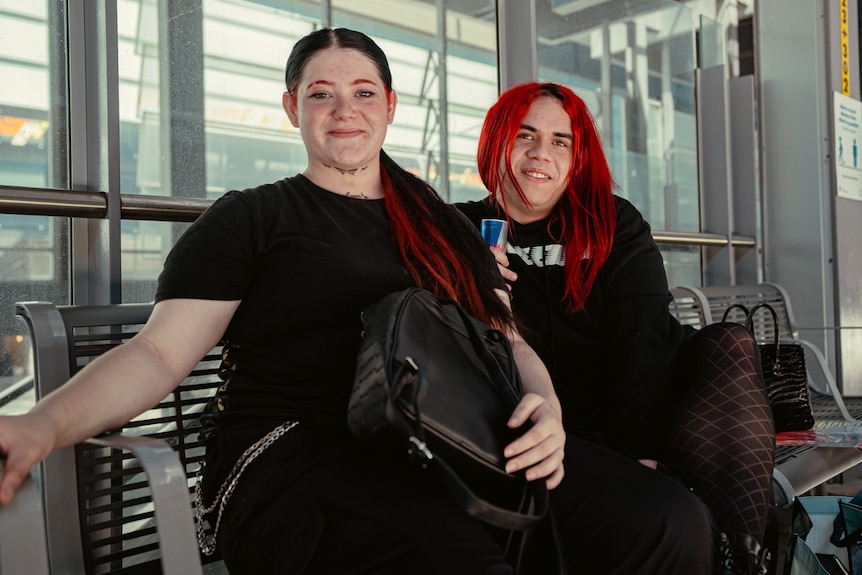 Two young people dressed in black sitting in a bus shelter.