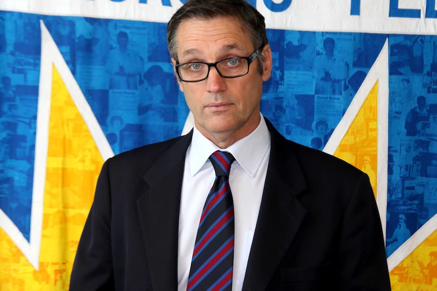 A mid shot of Mark olsen dressed in a suit and tie.