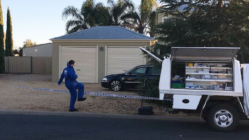 Woman dressed in blue plastic onesie steps over police tape into a property.