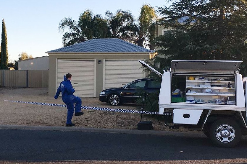 Woman dressed in blue plastic onesie steps over police tape into a property.